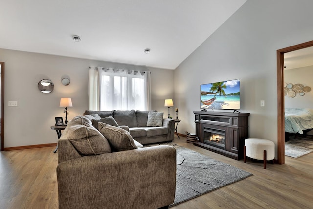 living area with light wood-style floors, baseboards, a glass covered fireplace, and lofted ceiling