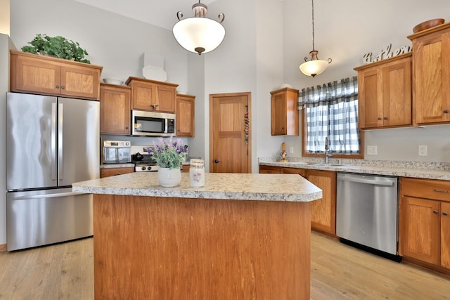 kitchen featuring a high ceiling, appliances with stainless steel finishes, a sink, light countertops, and light wood-type flooring