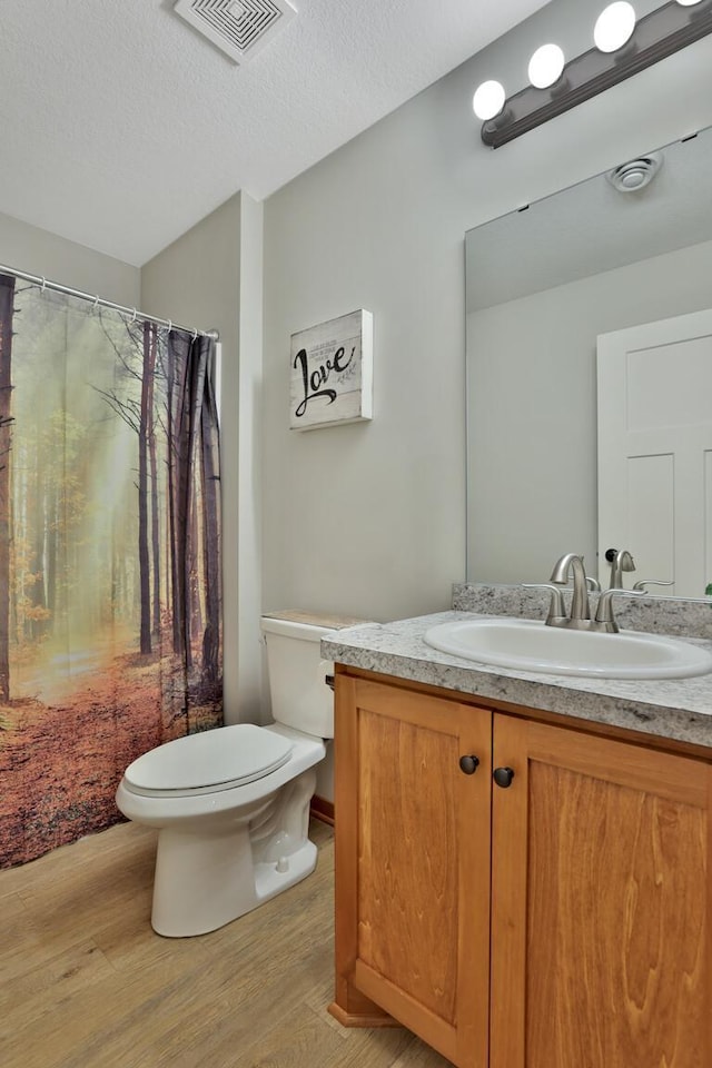 full bath with a textured ceiling, visible vents, wood finished floors, vanity, and toilet