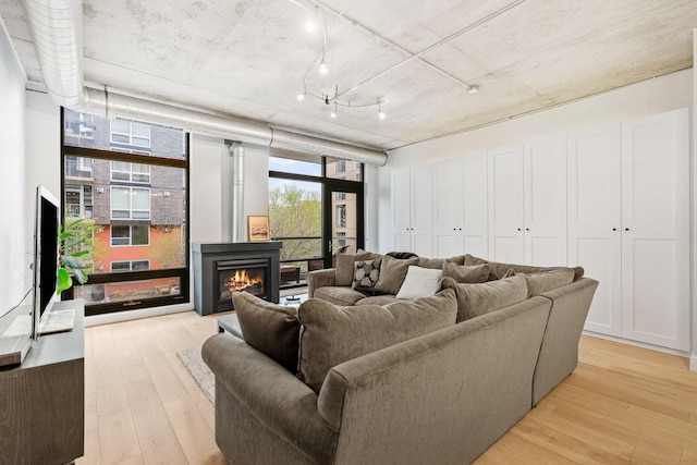 living area with a warm lit fireplace, floor to ceiling windows, and light wood finished floors