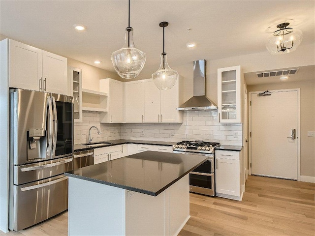 kitchen featuring wall chimney range hood, dark countertops, a sink, stainless steel appliances, and visible vents