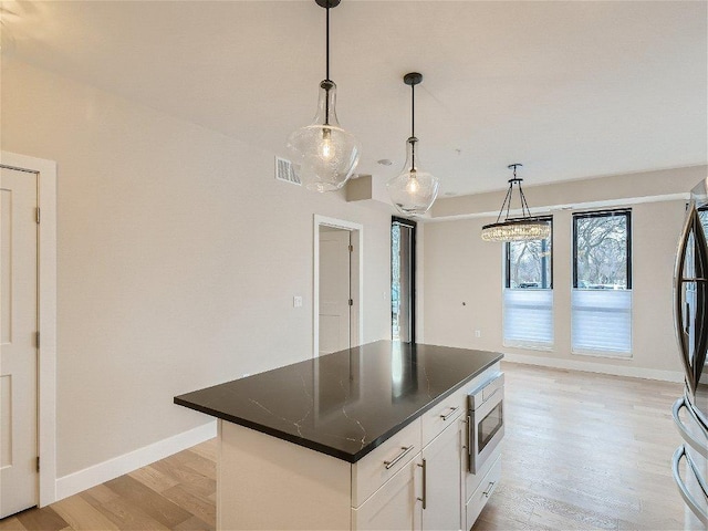 kitchen with a kitchen island, visible vents, dark countertops, appliances with stainless steel finishes, and light wood finished floors