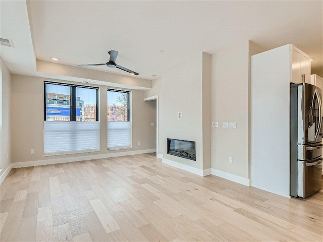 unfurnished living room featuring light wood-type flooring, a ceiling fan, baseboards, and visible vents