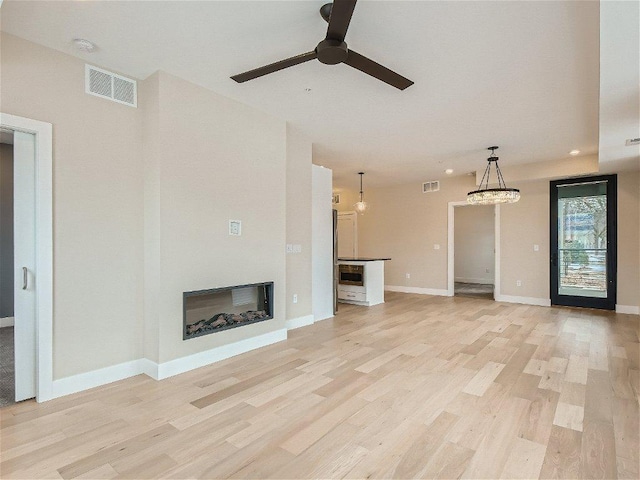 unfurnished living room with a glass covered fireplace, ceiling fan, light wood-style floors, and visible vents