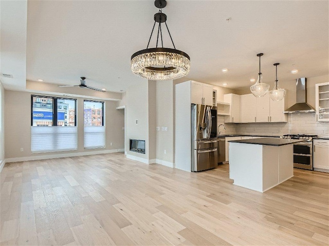 kitchen featuring dark countertops, light wood-style floors, wall chimney exhaust hood, stainless steel appliances, and backsplash