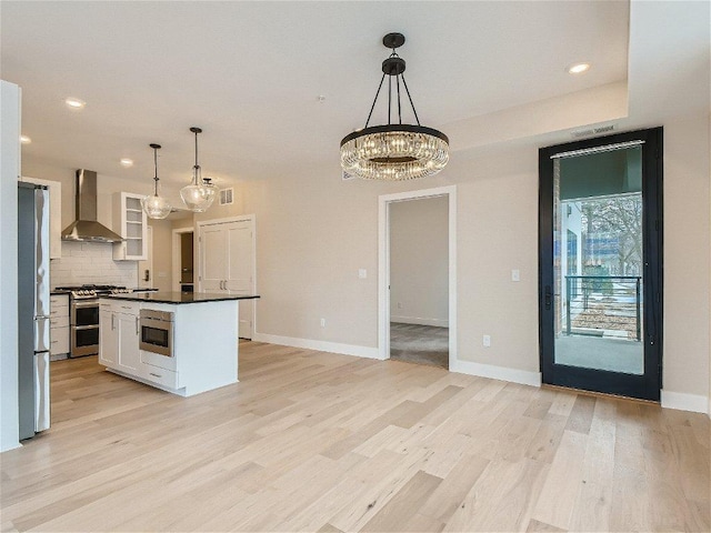 kitchen with dark countertops, wall chimney range hood, white cabinets, tasteful backsplash, and appliances with stainless steel finishes