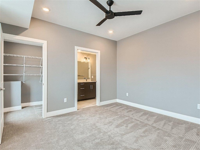 unfurnished bedroom with light carpet, a walk in closet, recessed lighting, baseboards, and a closet