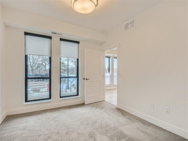 spare room featuring baseboards, light colored carpet, and visible vents