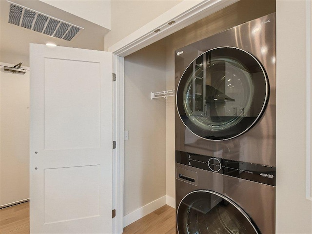 laundry area featuring laundry area, stacked washing maching and dryer, light wood-style flooring, baseboards, and visible vents