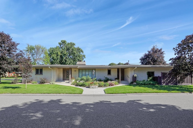 single story home featuring brick siding, a chimney, a front yard, and fence