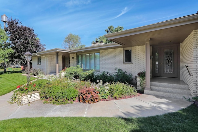 view of exterior entry featuring a lawn and brick siding