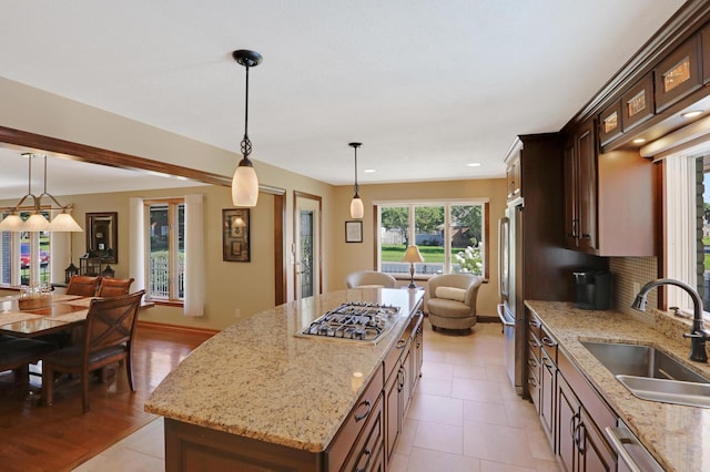 kitchen with dark brown cabinetry, appliances with stainless steel finishes, a sink, baseboards, and a kitchen island