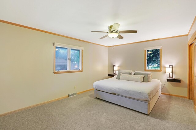 carpeted bedroom with visible vents, ornamental molding, baseboards, and ceiling fan