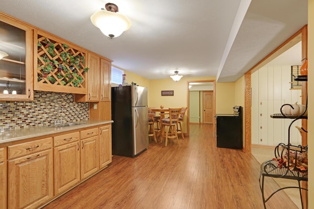 kitchen featuring freestanding refrigerator, light wood-style floors, light countertops, a sink, and backsplash