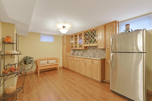 kitchen featuring freestanding refrigerator, light wood-type flooring, decorative backsplash, and light countertops