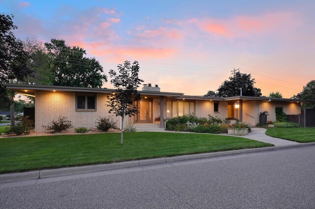 ranch-style home with brick siding, a chimney, and a front lawn