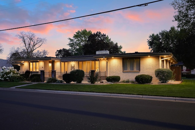 mid-century inspired home featuring brick siding, a chimney, a yard, and fence private yard