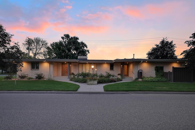 view of front of home featuring a lawn, brick siding, and fence