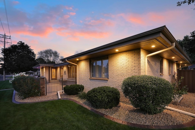 property exterior at dusk with brick siding, a lawn, and fence