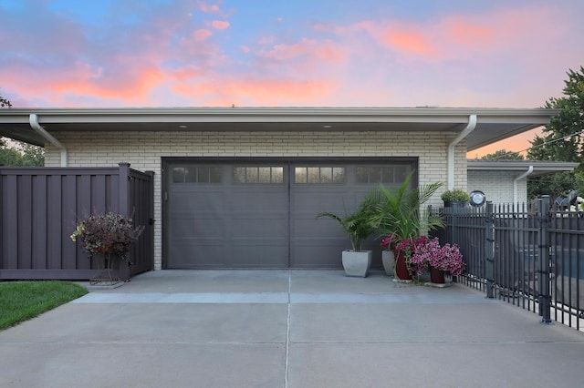 garage at dusk with fence and concrete driveway