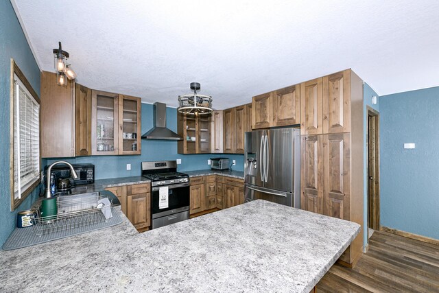 kitchen featuring a peninsula, wall chimney range hood, appliances with stainless steel finishes, and brown cabinetry