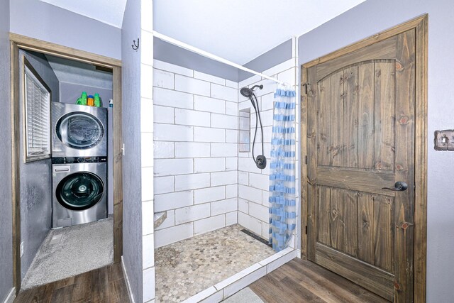 full bath featuring tiled shower, stacked washer and clothes dryer, and wood finished floors