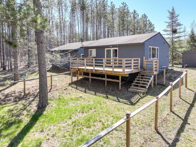 back of property featuring roof with shingles, a wooden deck, fence, and a lawn