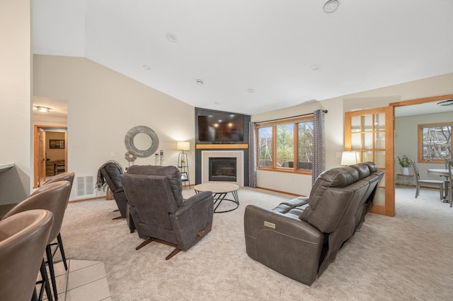 living room featuring light carpet, visible vents, a glass covered fireplace, baseboards, and vaulted ceiling