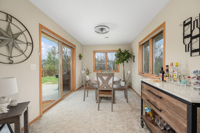 dining area with baseboards, a dry bar, and light carpet