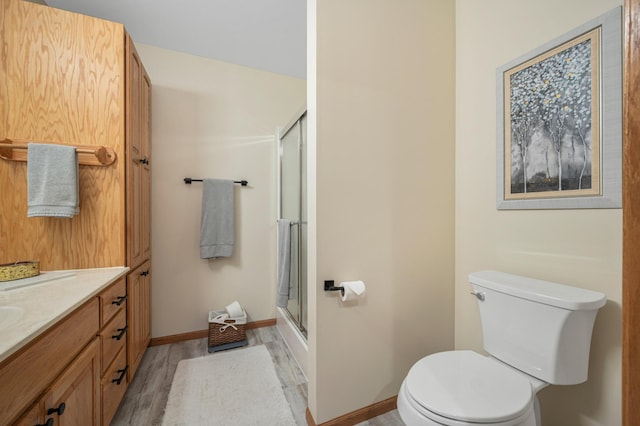 full bath featuring vanity, a shower with door, wood finished floors, toilet, and baseboards
