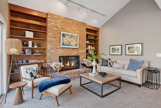 carpeted living room with rail lighting, a brick fireplace, and built in shelves