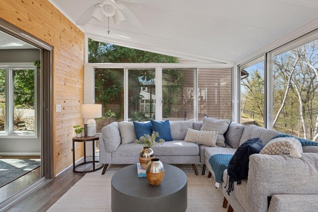sunroom / solarium featuring ceiling fan, vaulted ceiling, wood walls, and wood finished floors