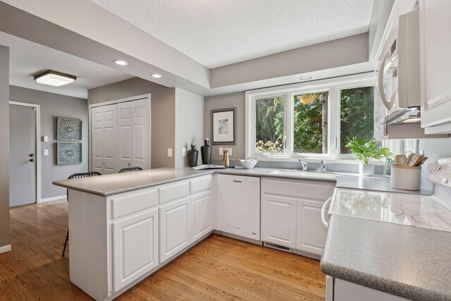 kitchen featuring white cabinets, a sink, light wood-style floors, white appliances, and a peninsula