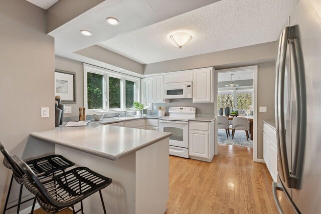 kitchen featuring white appliances, a peninsula, white cabinetry, and a kitchen breakfast bar