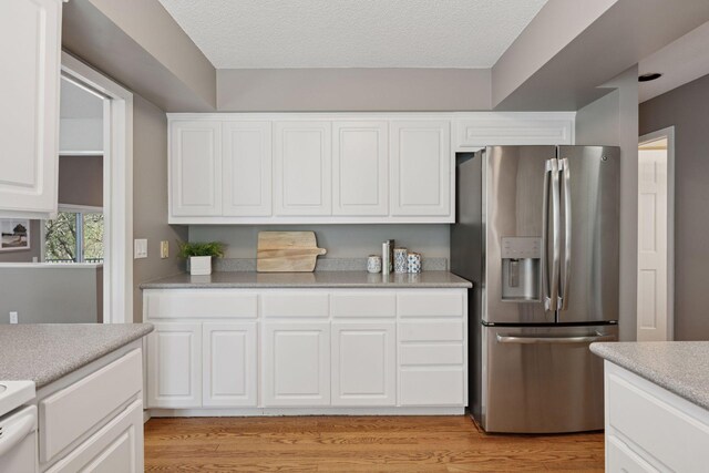 kitchen with stainless steel fridge, light countertops, a textured ceiling, white cabinetry, and light wood-style flooring