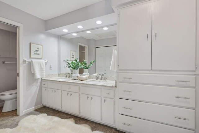 full bathroom featuring double vanity, a sink, baseboards, and toilet