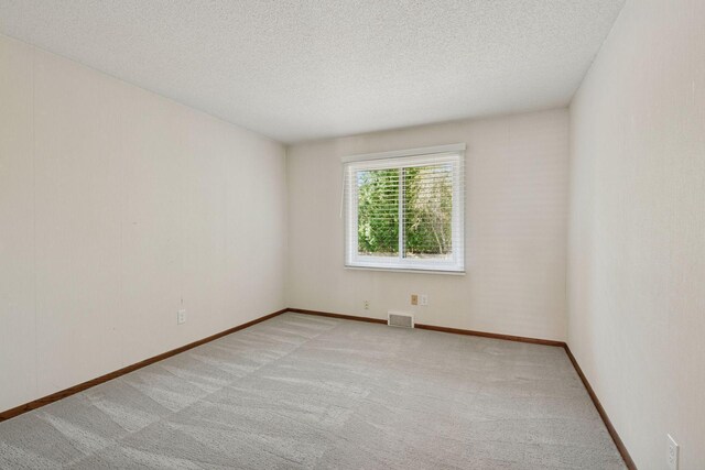 unfurnished room featuring a textured ceiling, visible vents, light carpet, and baseboards