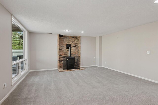 unfurnished living room featuring baseboards, a wood stove, and carpet flooring