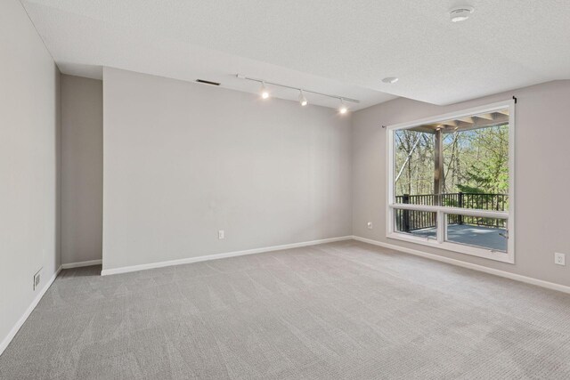 carpeted empty room featuring baseboards, rail lighting, a textured ceiling, and visible vents