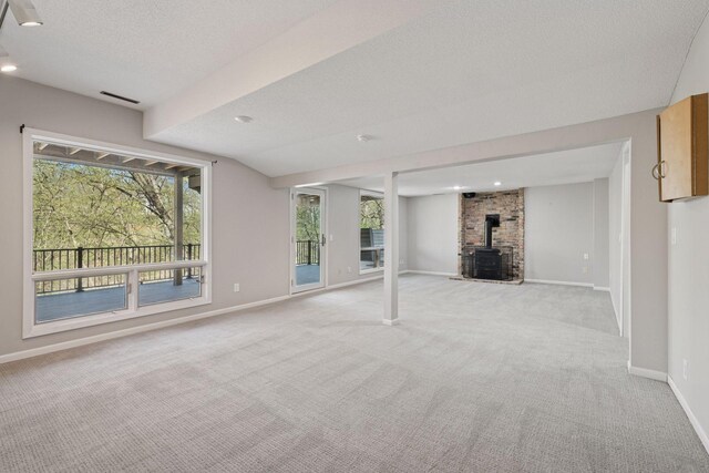 basement featuring a textured ceiling, baseboards, light colored carpet, and a wood stove