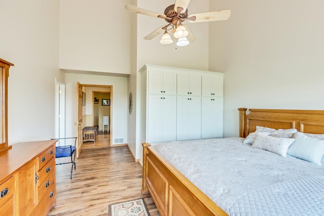 bedroom with a high ceiling, ceiling fan, light wood-type flooring, visible vents, and a closet