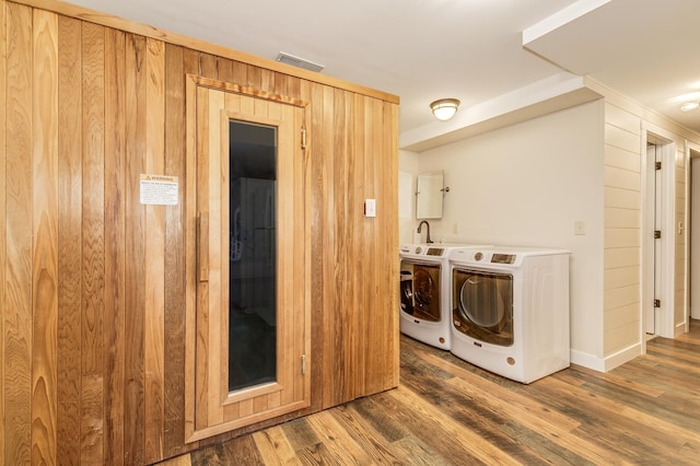 clothes washing area with independent washer and dryer, wooden walls, visible vents, and wood finished floors