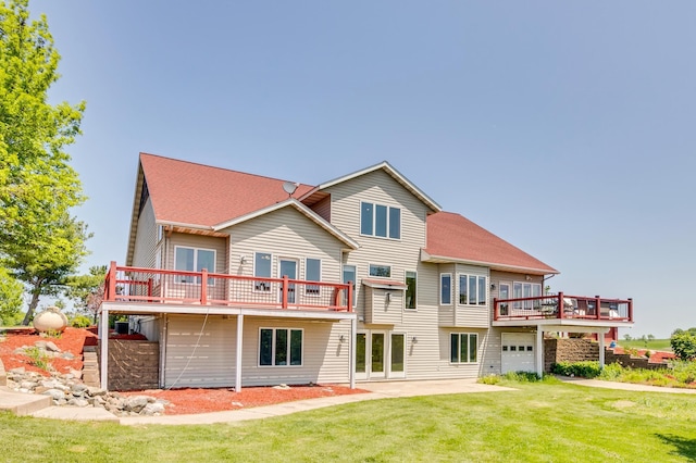 rear view of property featuring roof with shingles, a garage, a wooden deck, a patio area, and a lawn