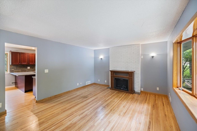 7872 142nd St W, Apple Valley, MN 55124 - unfurnished living room featuring light wood-style flooring, a brick fireplace, and a textured ceiling