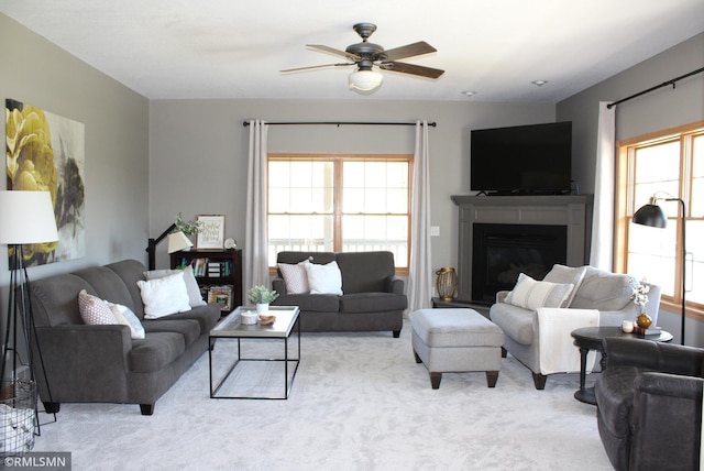 living area with a glass covered fireplace, ceiling fan, and carpet