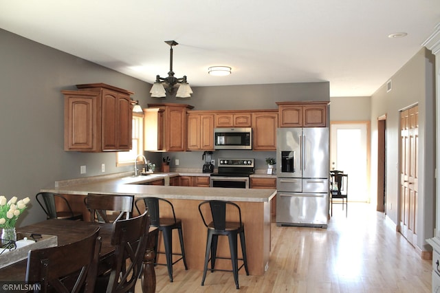 kitchen with light countertops, stainless steel appliances, light wood-type flooring, and a peninsula