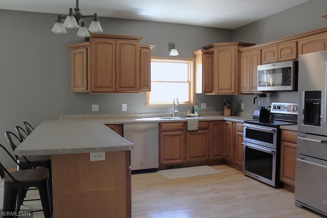 kitchen with a sink, a peninsula, a breakfast bar, stainless steel appliances, and light wood-style flooring