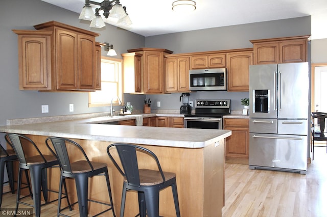 kitchen with a peninsula, a breakfast bar, light wood-type flooring, light countertops, and stainless steel appliances
