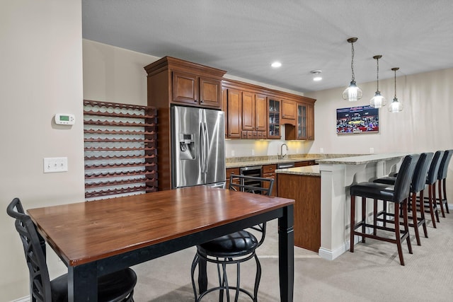 5435 Yellowstone Trl, Minnetrista, MN 55331 - kitchen featuring stainless steel refrigerator with ice dispenser, a kitchen bar, glass insert cabinets, brown cabinetry, and pendant lighting