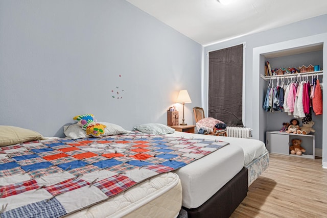bedroom featuring radiator heating unit, vaulted ceiling, a closet, and light wood-style flooring